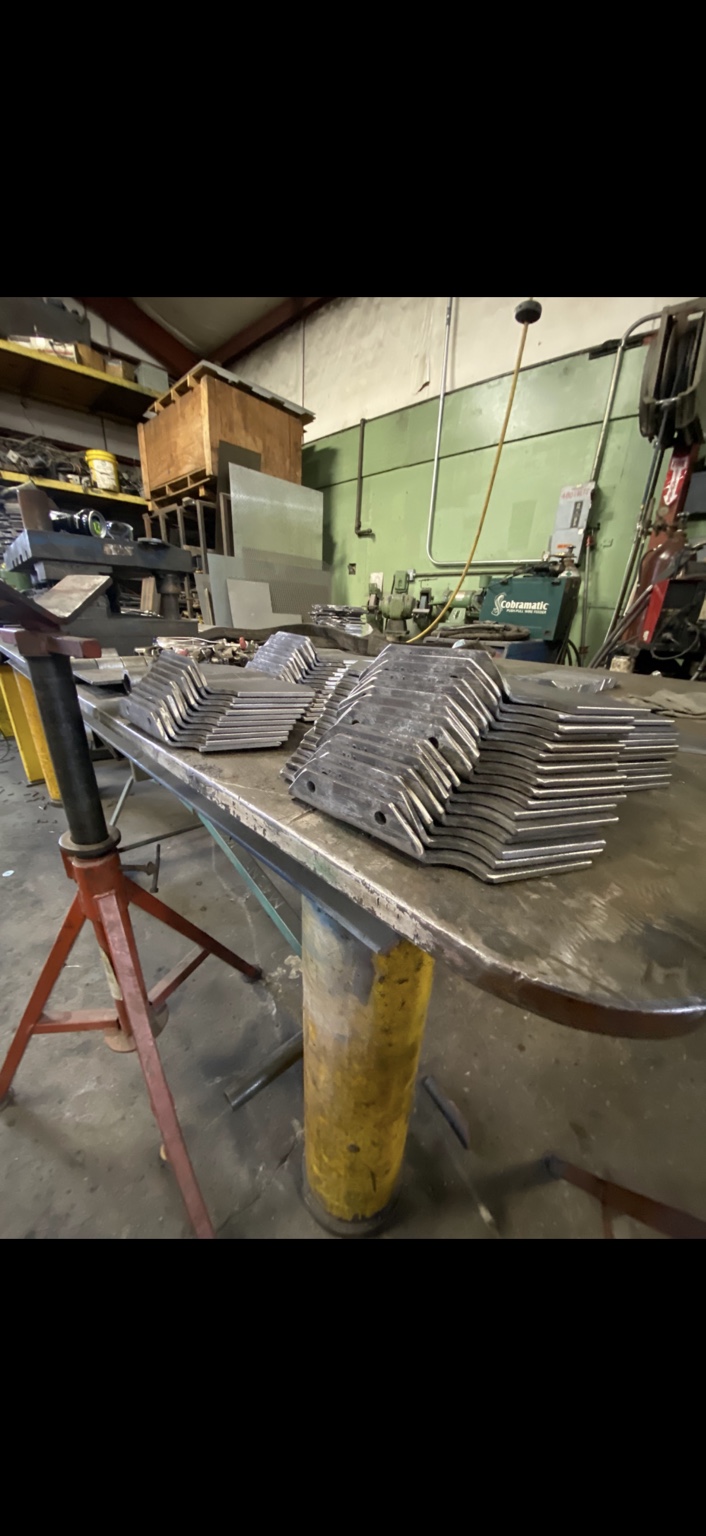 Stacks of formed steel conveyor parts with mounting holes on the shop workbench