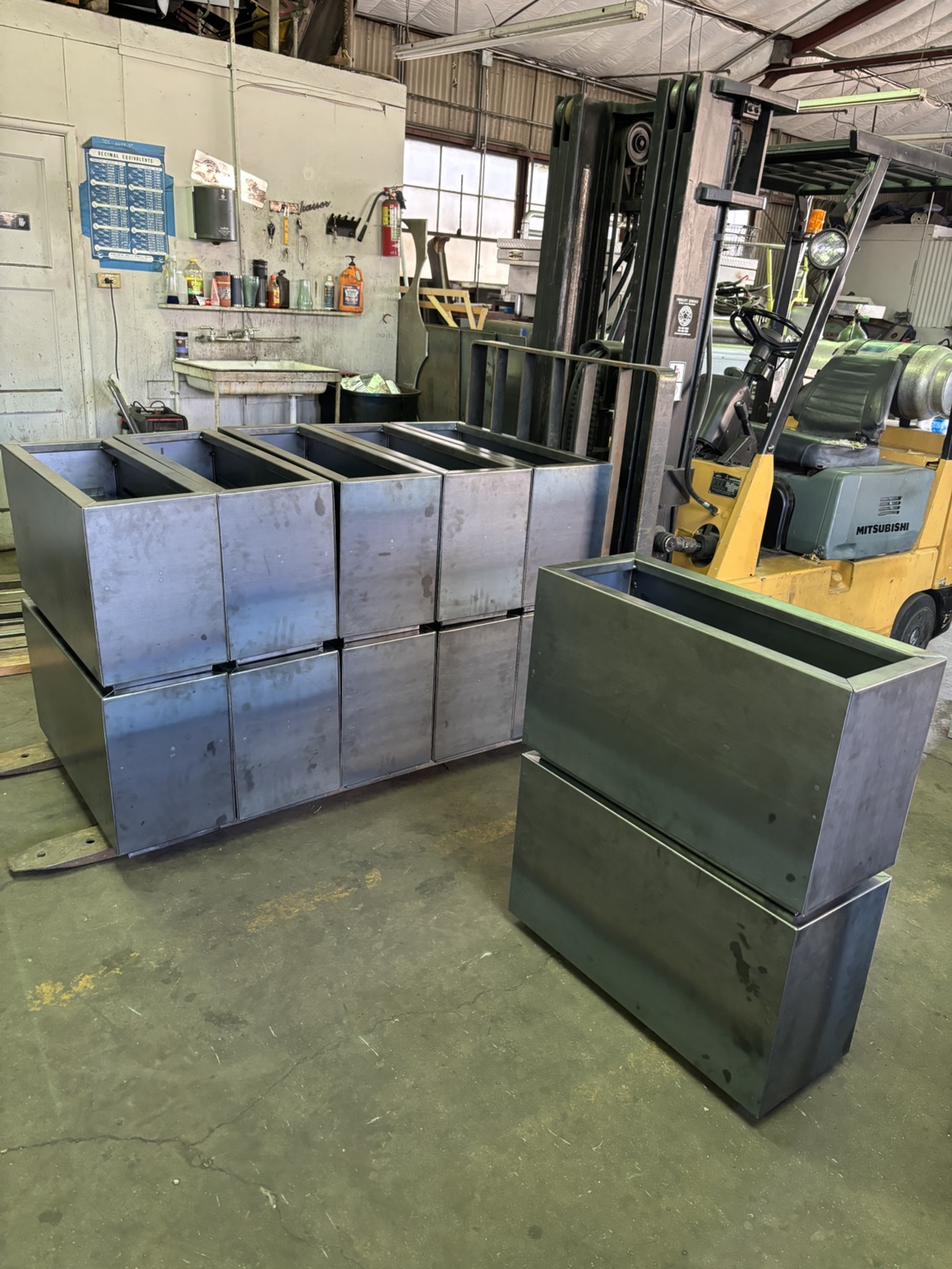 Multiple matching fabricated steel assemblies stacked beside a forklift